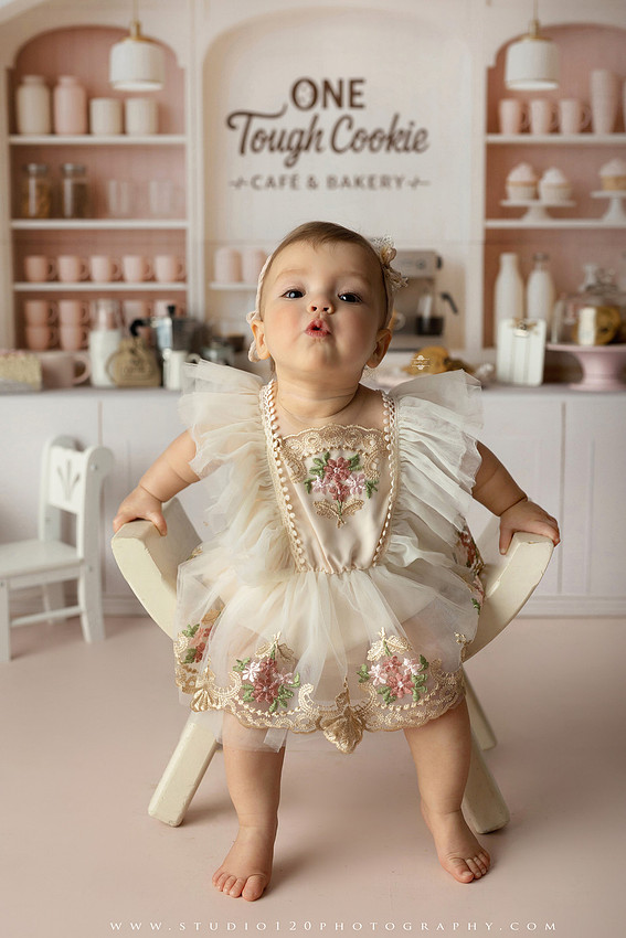 One Tough Cookie first birthday cake smash photography session featuring a baby girl in a soft pink bakery-themed set, chef outfit, floral dress, cookies, birthday cake and cake smash portraits at Studio 120 Photography in Ramona, California.