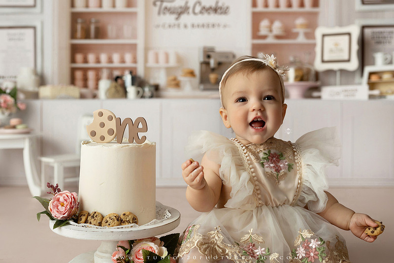 One Tough Cookie first birthday cake smash photography session featuring a baby girl in a soft pink bakery-themed set, chef outfit, floral dress, cookies, birthday cake and cake smash portraits at Studio 120 Photography in Ramona, California.