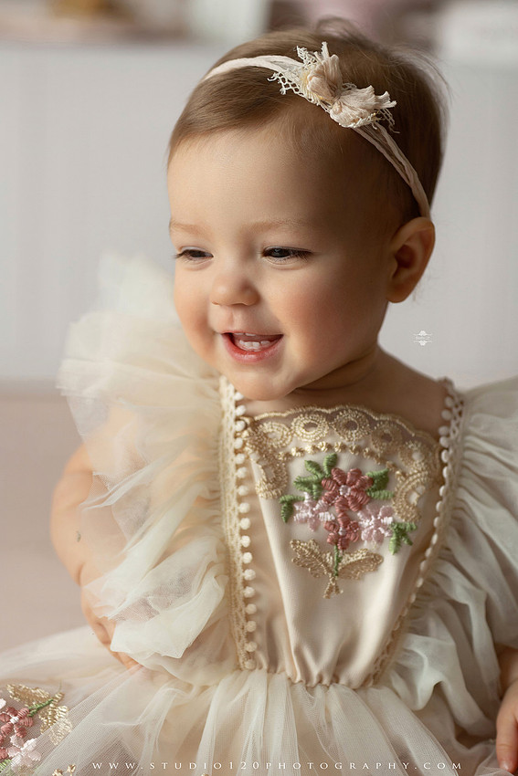 One Tough Cookie first birthday cake smash photography session featuring a baby girl in a soft pink bakery-themed set, chef outfit, floral dress, cookies, birthday cake and cake smash portraits at Studio 120 Photography in Ramona, California.