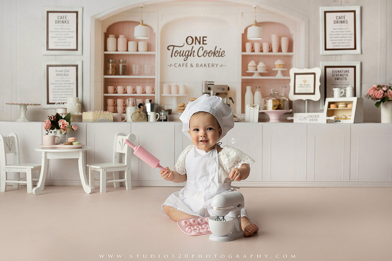 One Tough Cookie first birthday cake smash photography session featuring a baby girl in a soft pink bakery-themed set, chef outfit, floral dress, cookies, birthday cake and cake smash portraits at Studio 120 Photography in Ramona, California.