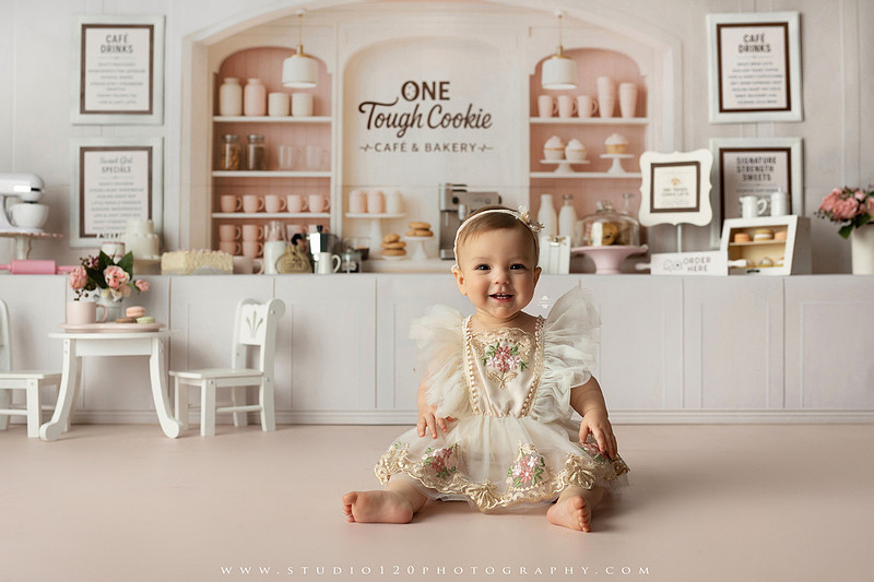 One Tough Cookie first birthday cake smash photography session featuring a baby girl in a soft pink bakery-themed set, chef outfit, floral dress, cookies, birthday cake and cake smash portraits at Studio 120 Photography in Ramona, California.