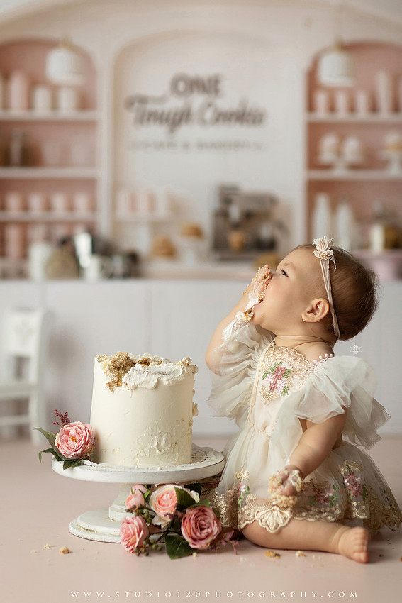 One Tough Cookie first birthday cake smash photography session featuring a baby girl in a soft pink bakery-themed set, chef outfit, floral dress, cookies, birthday cake and cake smash portraits at Studio 120 Photography in Ramona, California.