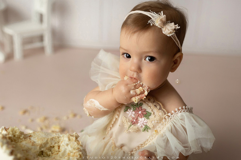 One Tough Cookie first birthday cake smash photography session featuring a baby girl in a soft pink bakery-themed set, chef outfit, floral dress, cookies, birthday cake and cake smash portraits at Studio 120 Photography in Ramona, California.