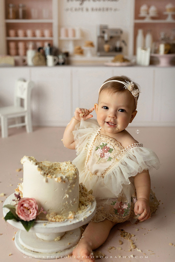 One Tough Cookie first birthday cake smash photography session featuring a baby girl in a soft pink bakery-themed set, chef outfit, floral dress, cookies, birthday cake and cake smash portraits at Studio 120 Photography in Ramona, California.