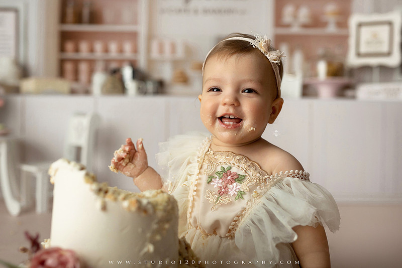 One Tough Cookie first birthday cake smash photography session featuring a baby girl in a soft pink bakery-themed set, chef outfit, floral dress, cookies, birthday cake and cake smash portraits at Studio 120 Photography in Ramona, California.