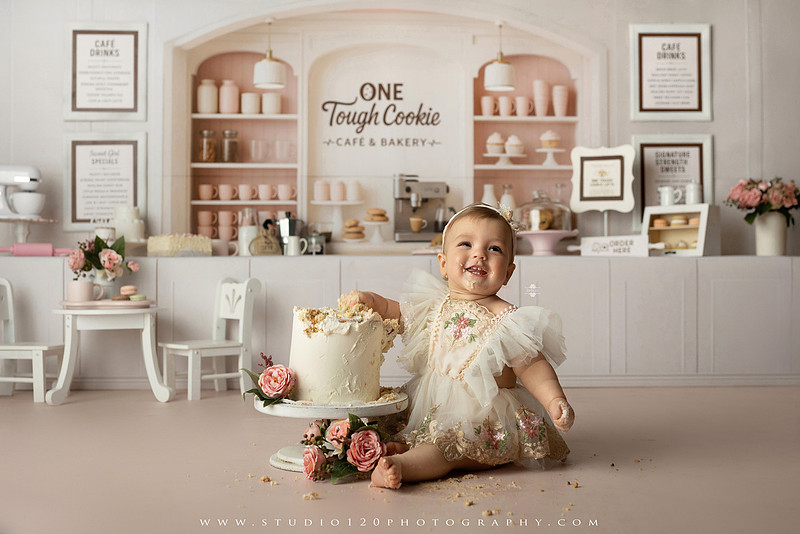 One Tough Cookie first birthday cake smash photography session featuring a baby girl in a soft pink bakery-themed set, chef outfit, floral dress, cookies, birthday cake and cake smash portraits at Studio 120 Photography in Ramona, California.