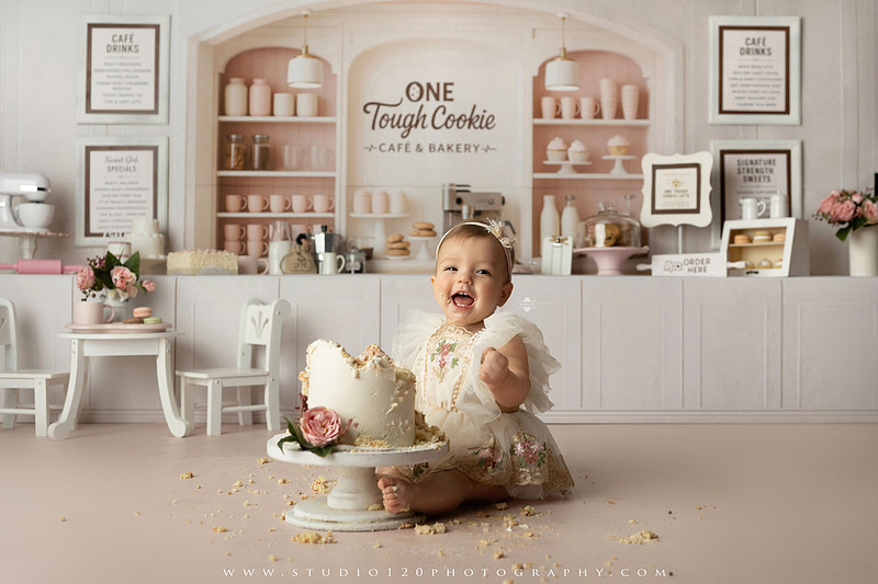 One Tough Cookie first birthday cake smash photography session featuring a baby girl in a soft pink bakery-themed set, chef outfit, floral dress, cookies, birthday cake and cake smash portraits at Studio 120 Photography in Ramona, California.