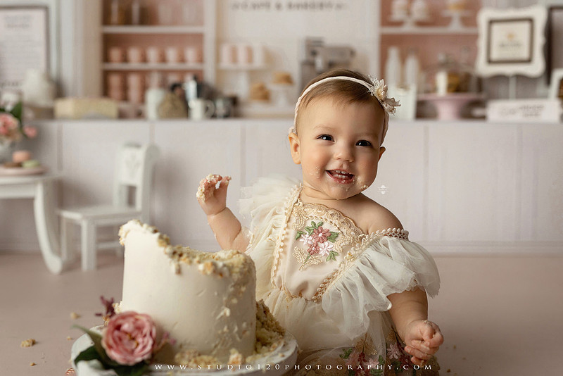 One Tough Cookie first birthday cake smash photography session featuring a baby girl in a soft pink bakery-themed set, chef outfit, floral dress, cookies, birthday cake and cake smash portraits at Studio 120 Photography in Ramona, California.