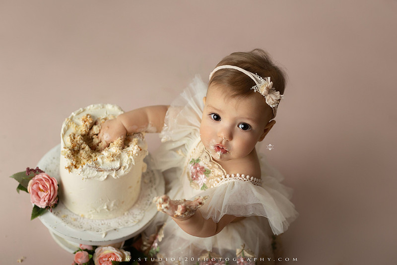 One Tough Cookie first birthday cake smash photography session featuring a baby girl in a soft pink bakery-themed set, chef outfit, floral dress, cookies, birthday cake and cake smash portraits at Studio 120 Photography in Ramona, California.