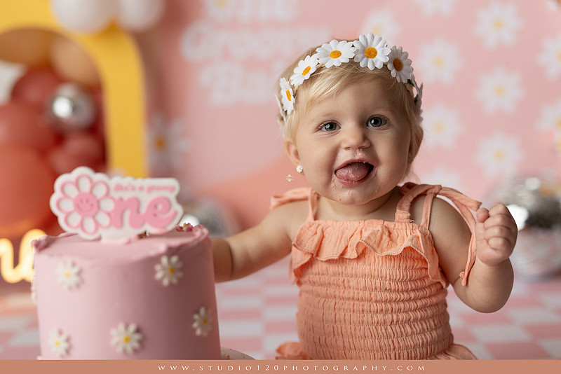 One Groovy Babe first birthday cake smash photography session at Studio 120 Photography in Ramona, California, featuring a baby girl in a pink and yellow retro daisy and disco themed set with balloons, a pink birthday cake, flower crown and vintage groovy van, followed by a rustic apple milk bath with red apples, florals and wooden accents.