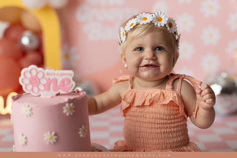 One Groovy Babe first birthday cake smash photography session at Studio 120 Photography in Ramona, California, featuring a baby girl in a pink and yellow retro daisy and disco themed set with balloons, a pink birthday cake, flower crown and vintage groovy van, followed by a rustic apple milk bath with red apples, florals and wooden accents.