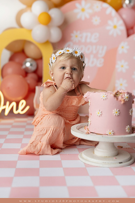 One Groovy Babe first birthday cake smash photography session at Studio 120 Photography in Ramona, California, featuring a baby girl in a pink and yellow retro daisy and disco themed set with balloons, a pink birthday cake, flower crown and vintage groovy van, followed by a rustic apple milk bath with red apples, florals and wooden accents.