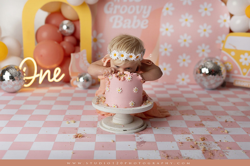 One Groovy Babe first birthday cake smash photography session at Studio 120 Photography in Ramona, California, featuring a baby girl in a pink and yellow retro daisy and disco themed set with balloons, a pink birthday cake, flower crown and vintage groovy van, followed by a rustic apple milk bath with red apples, florals and wooden accents.